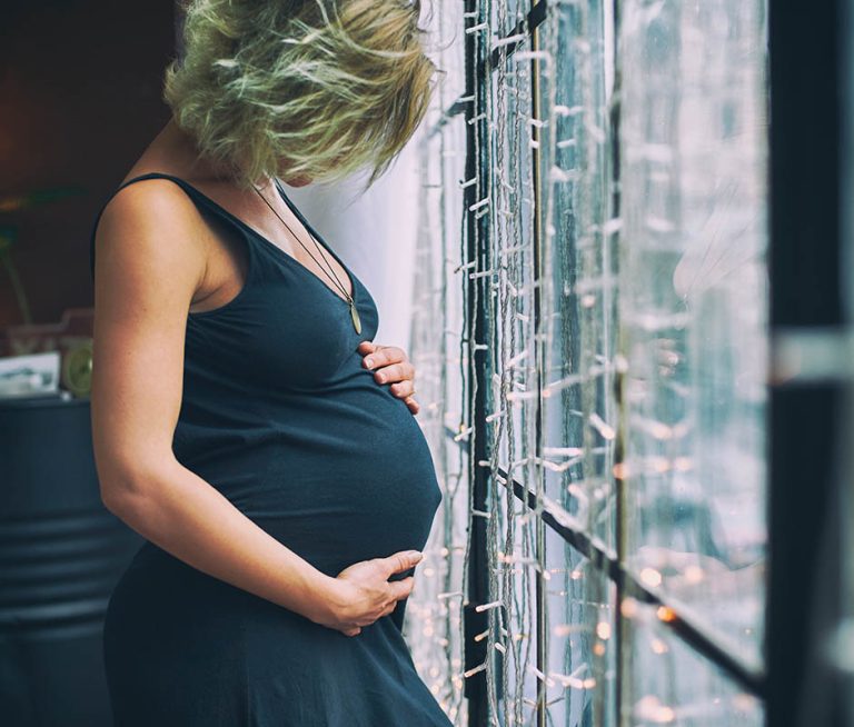 Young beautiful pregnant woman standing near window